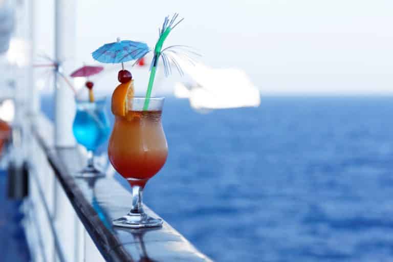 Colorful fruity cruise drinks with umbrellas, reminiscent of tropical paradise, perfectly positioned on the railing of a cruise ship. DIY cruise drink recipes bring a taste of the high seas to your home.