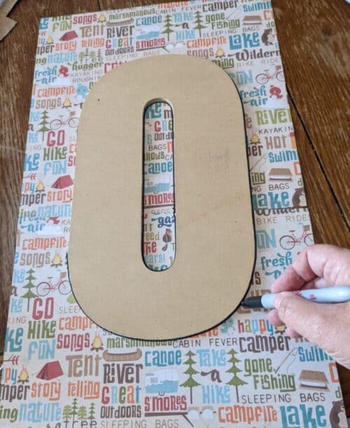 Large wooden letter O sits atop scrapbook paper being traced with a sharpy marker