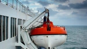 orange and white lifeboat hangs on side of white cruise ship