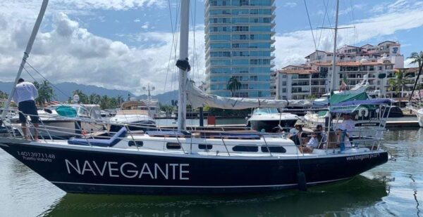 A blue and white sailboat, the Navagante XL sits at dock as crew clean and organized for next sailing.