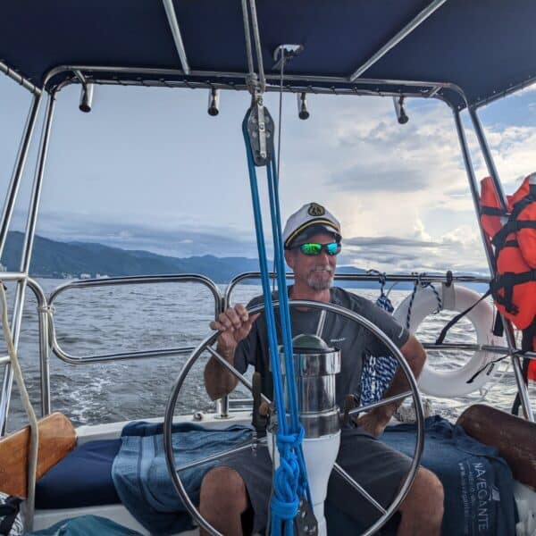 Man in gray shorts and blue shirt sleeved shirt beems as he steers the sailboat on his birthday trip. Gallivanting Souls chartered a sailboat in Puerto Vallarta
