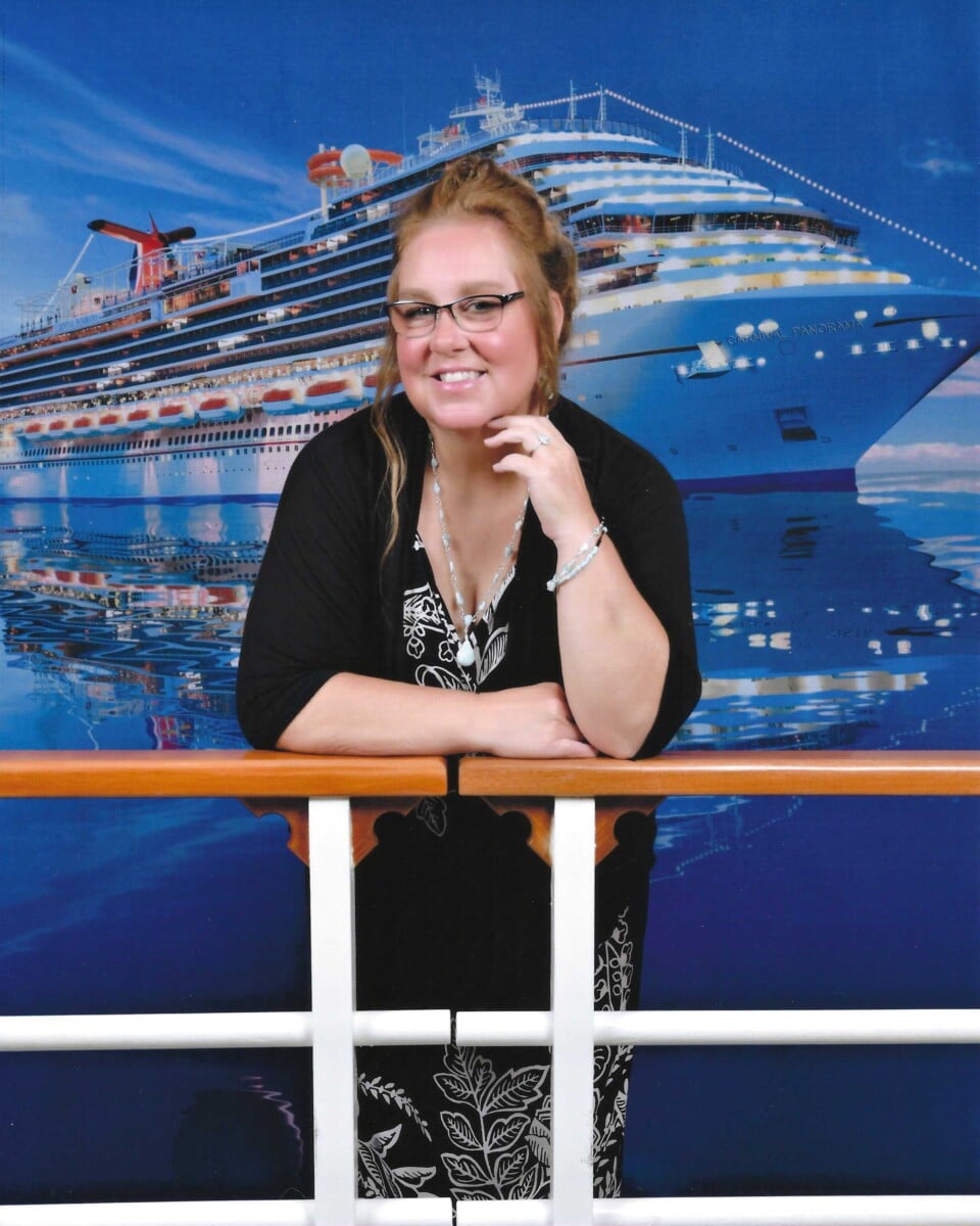 Woman poses in front of cruise ship backdrop, leaning on a railing.