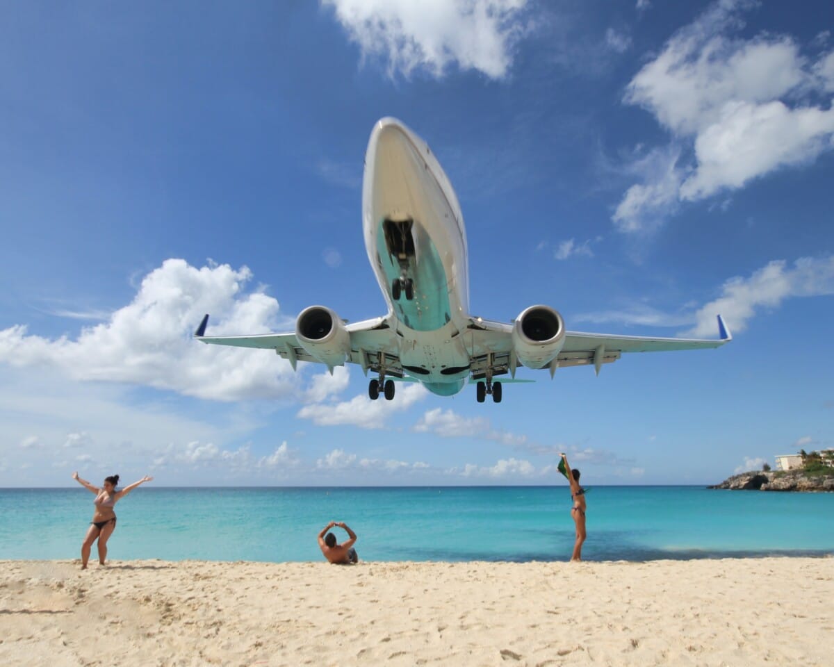 Huge jet flies over beach goers at Sint Maarten blue ocean and sand and people posing