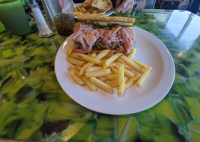 Golden fried french fries on a white plate with a panini pressed bread and several types of pork and pickles at Carnival Deli