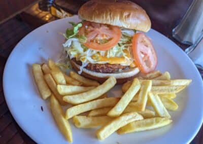 golden french fries on a white dinner plate next to a hamburger bun with lettuce, tomato, melty orange cheese, and a veggie burger from Carnival Deli.