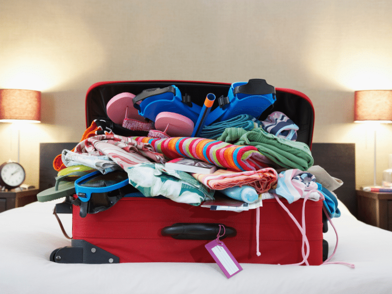 red suitcase on bed is overflowing with clothes and toys