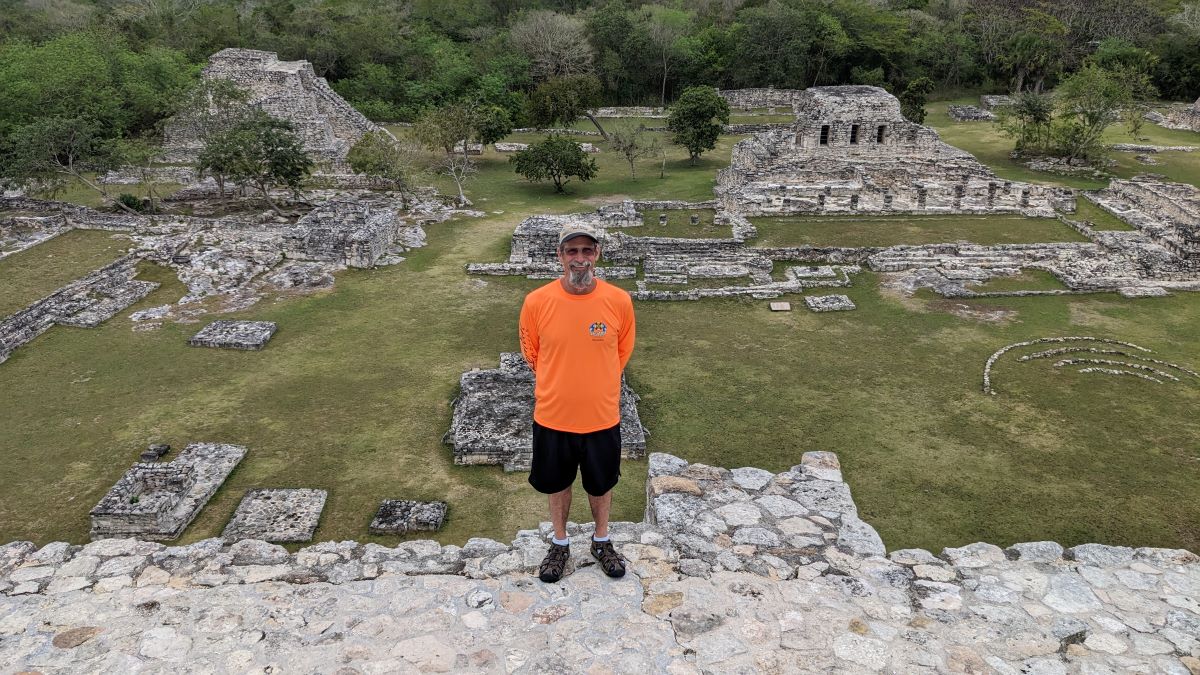 man in orange shirt and black shorts poses on top of the Mayapan Ruins near Yucatan, Progresso, Mexico from his Carnival Valor Cruise