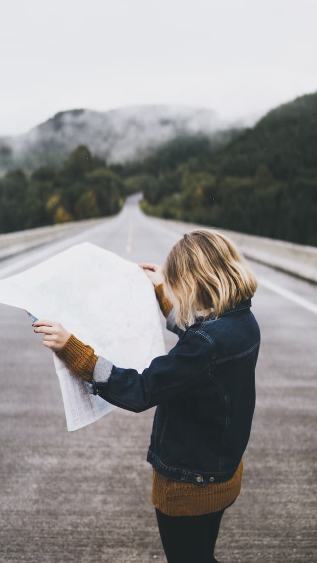 woman stands on road with open map feeling lost.