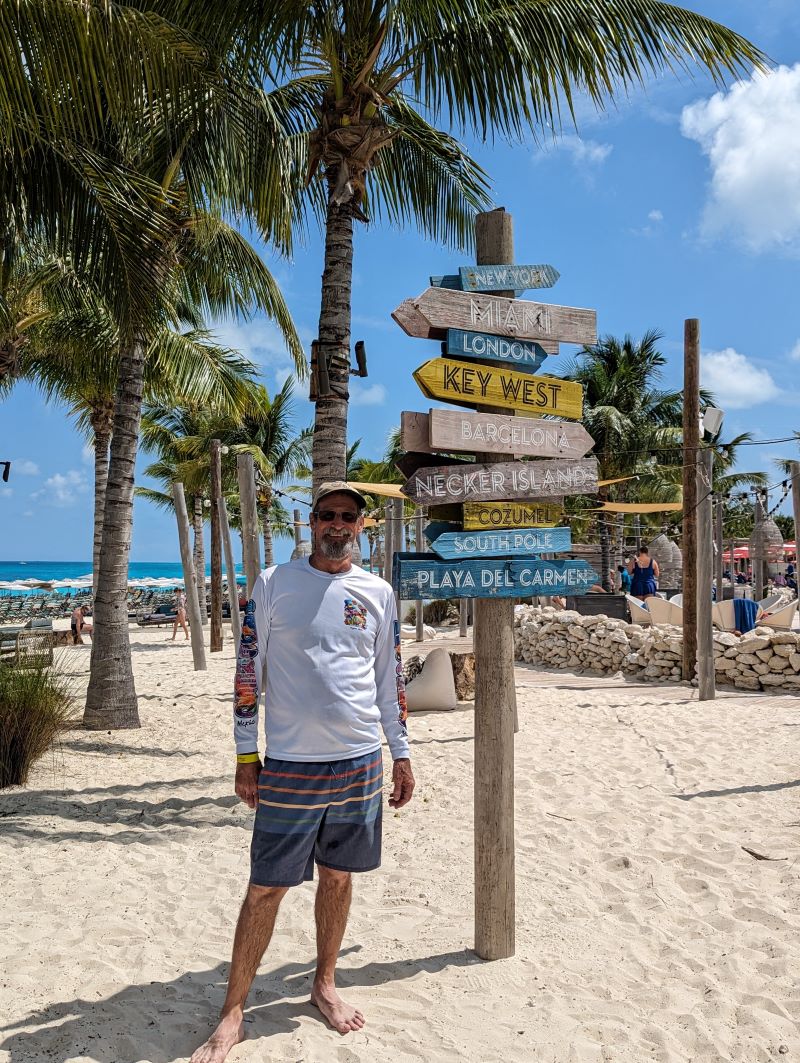 Man poses in front of signs pointing to far off destinations at Beach 360 resort.