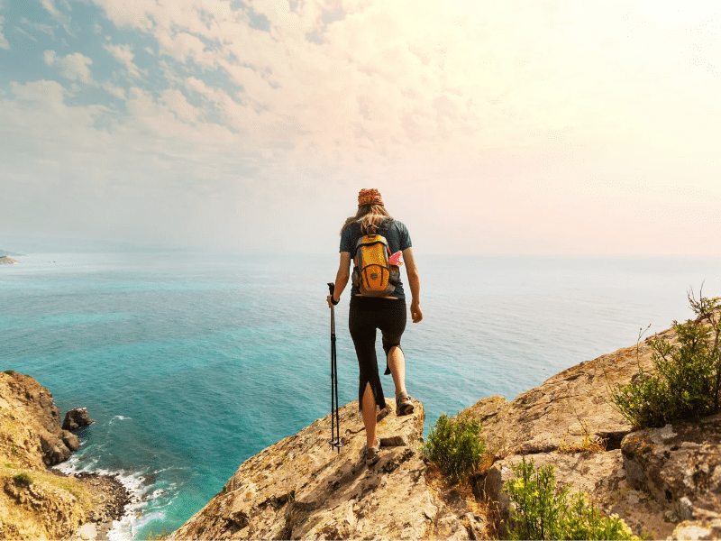 Woman on a hike stand at edge of cliff to admire the view on a cruise port day hike