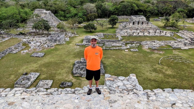 man in orange shirt stands at yucatan ruins