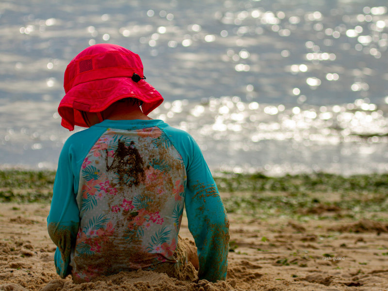 Little girl plays in sand protected from sun with a hat and rash guard