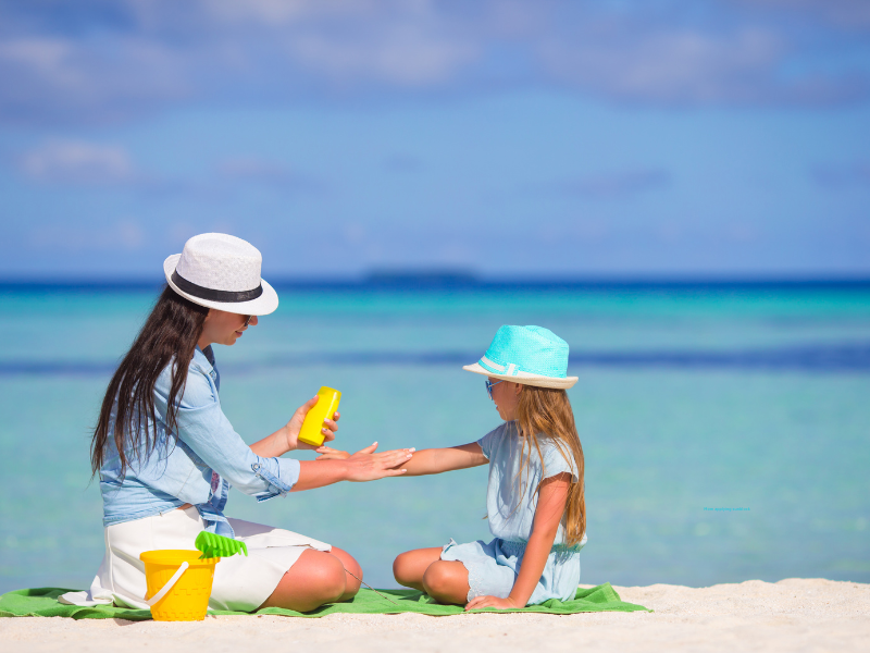 Mom applies sun block to her daughter at the beach.