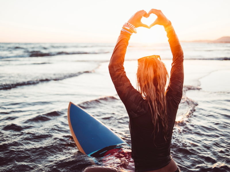 Woman on surf board is happy because she won't get sunburned because she is wearing a sun shirt for  protecting her skin against sun burn