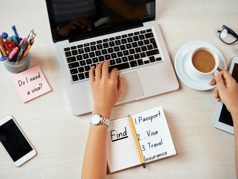 Hands on a computer screen and handwritten notes to find out about Passports,visas, and travel insurance.