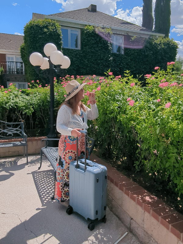 greenwich pro med roses Woman in colorful dress stops to smell the roses with her blue suitcase