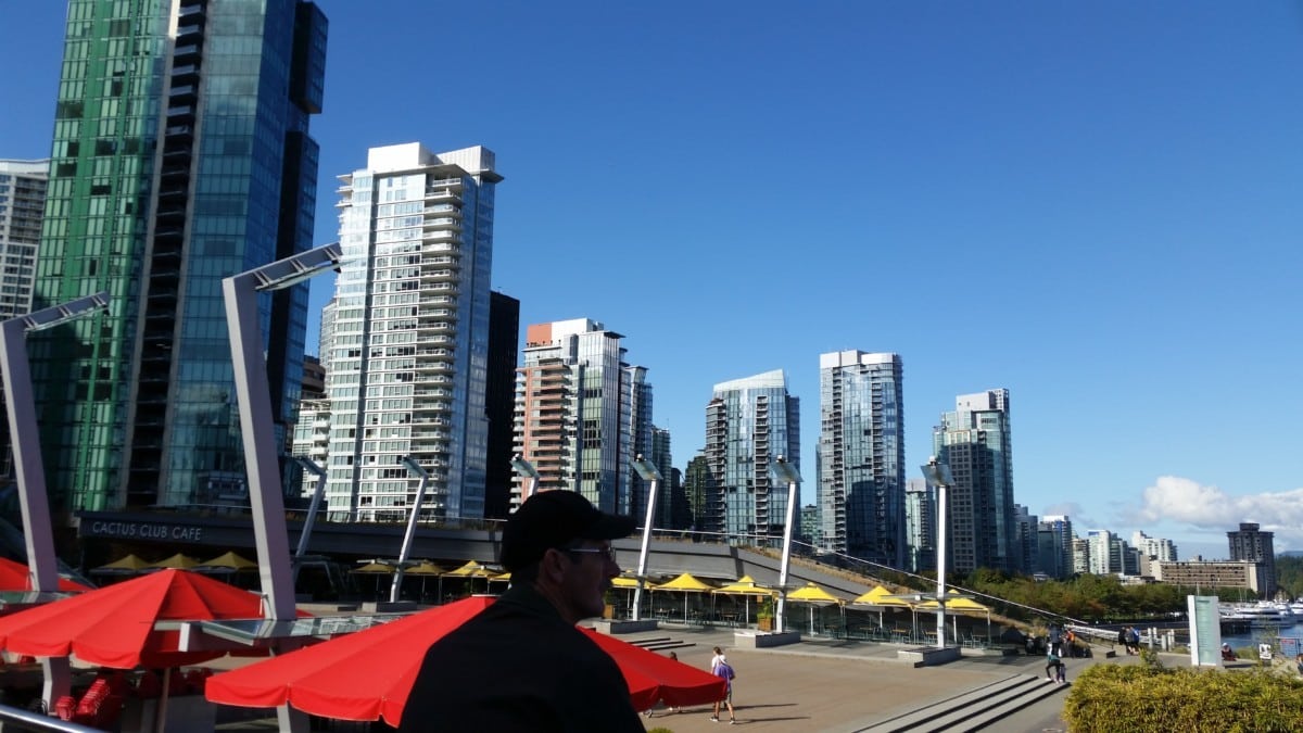 Man in hat stand next to skyline at waterfront area in Vancouver British Columbia